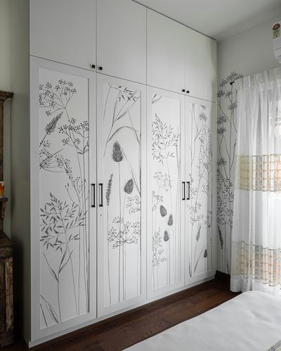 White wardrobe with botanical line drawings beside sheer curtain and wood floor in bedroom