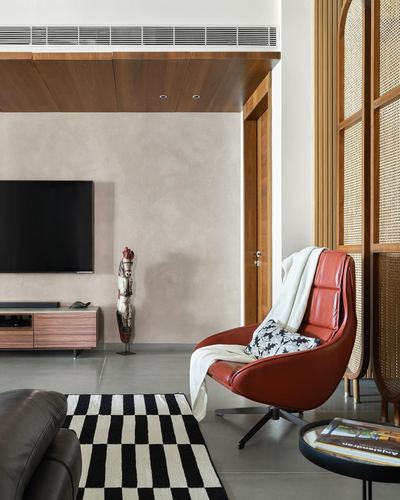 Living room corner with rust leather swivel chair, checkered rug, and cane room divider beside TV console