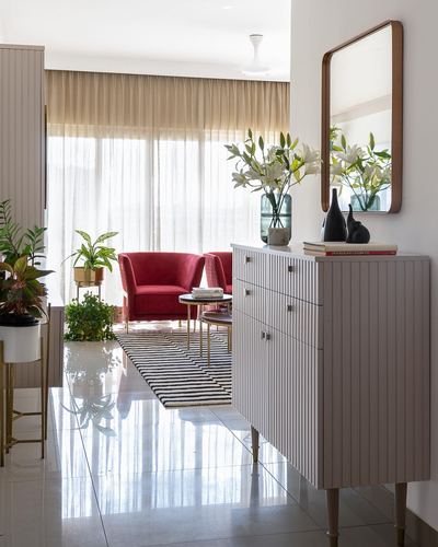 Foyer with fluted cabinet, arched mirror, and lilies leading into a living room with red chairs