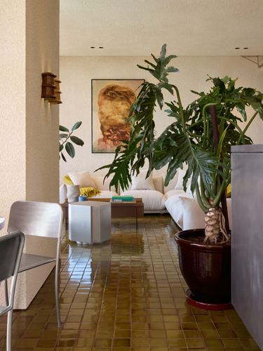 Living room with glazed olive tile floor, large philodendron, white sofa, and portrait painting