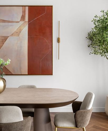 Oval dining table with upholstered chairs beneath a large abstract painting and brass sconce