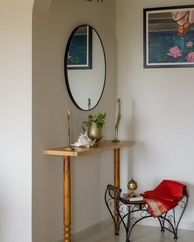Foyer niche with round mirror over a wooden console styled with brass objects and a red-draped iron stool
