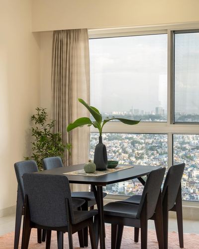 Dining table with grey upholstered chairs facing a floor-to-ceiling window overlooking a city skyline