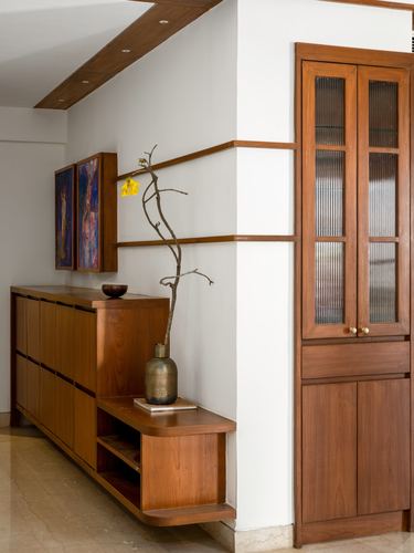 Wooden console and tall fluted-glass cabinet in a warm-toned entry corner with a brass vase and dried branch.