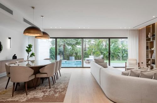 Open living-dining space with dome pendants, curved sofa, and glass doors framing a garden and pool