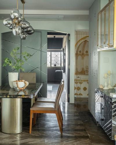 Green paneled dining area with marble table and cluster pendant light leading to gold-detailed passage
