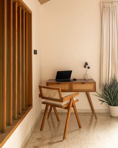 Wooden study desk with cane chair beside a slatted timber partition and stone floor