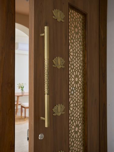 Close-up of a wooden entrance door with brass handle, lotus motifs, and a carved jali panel.