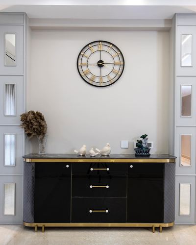 Black and gold sideboard below a large wall clock, flanked by mirrored recessed niches