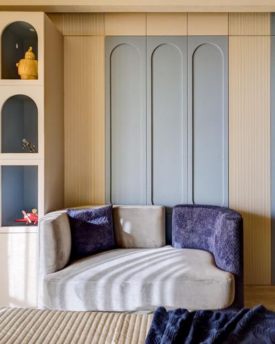 Curved beige sofa with purple cushions beside arched shelving and fluted paneled wardrobe