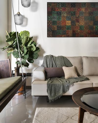Cream sofa with green throw beneath patchwork wall art beside a fiddle leaf fig plant