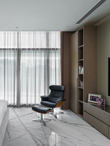 Black leather lounge chair and ottoman beside sheer curtained window in modern bedroom with wood shelving