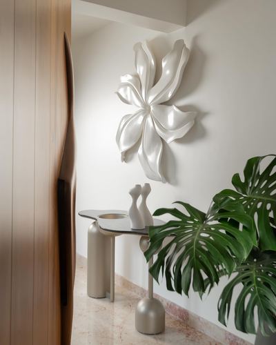 White biomorphic wall sculpture above a curved console table with monstera plant, fluted wood door beside it