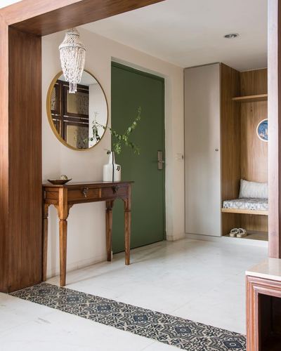 Entryway with round mirror over wooden console, green door, and patterned runner on marble floor