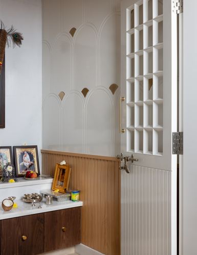 Pooja corner with arched fluted wall panels, wood cabinetry, and a lattice grille door