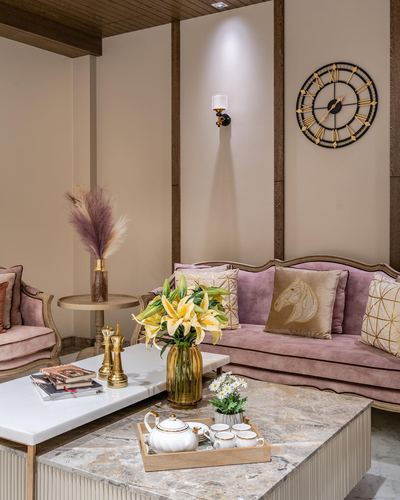 Pink velvet tufted sofa with gold cushions beside marble coffee table and round wall clock