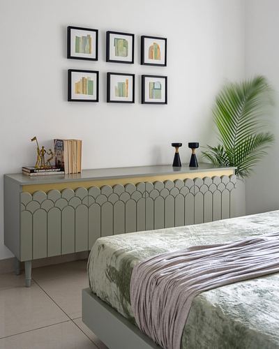 Sage green scalloped sideboard below gallery wall in bedroom with palm plant and bed foreground