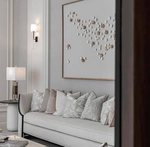Beige sofa with textured pillows beneath framed dotted wall art and a brass wall sconce