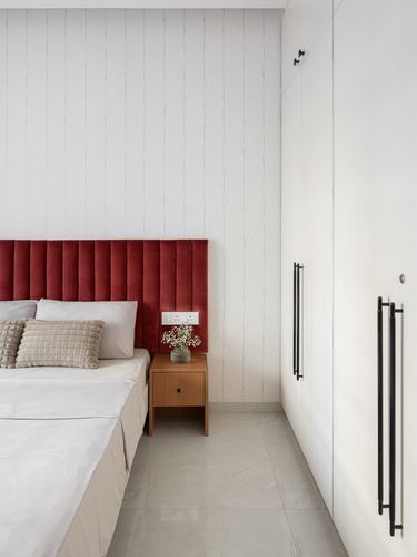Bedroom corner with maroon channel-tufted headboard, wooden nightstand, and white wardrobe with black handles