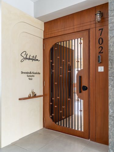 Curved wooden entrance door with metal grille beside cream wall bearing family name signage