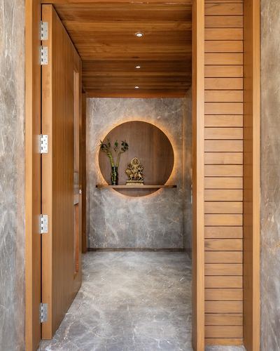 Foyer corridor leading to a backlit circular wooden niche holding a brass idol