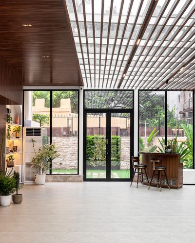 Glasshouse entry with wood-slat ceiling, black-framed glass walls, and a wooden bar corner opening to a garden