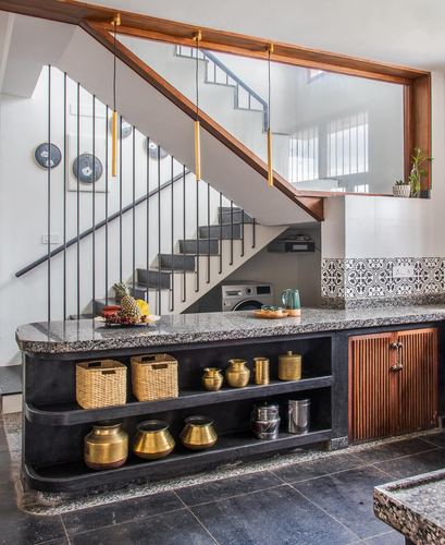 Curved granite counter with brass pots and baskets beneath an open staircase