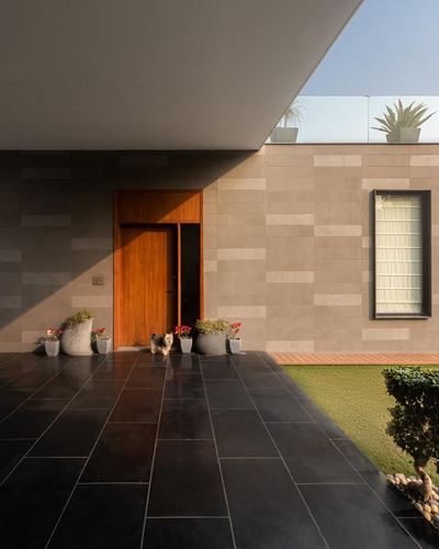 House entrance with wooden door, stone cladding, black tiled floor, dog standing near planters