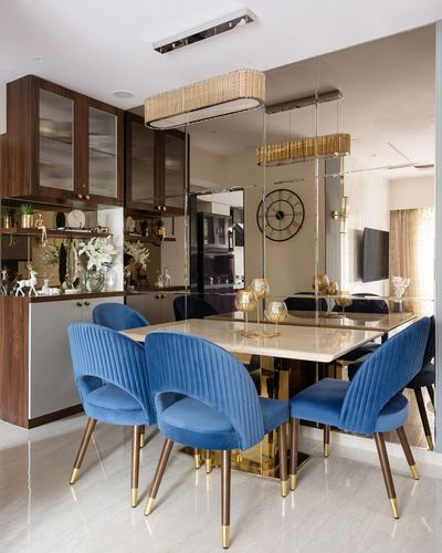 Dining table with blue velvet chairs and gold pendant lights against mirrored wall