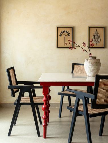 Dining set with black cane chairs and red-legged stone-top table against a mustard textured wall
