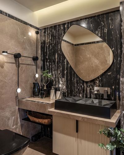 Bathroom vanity with faceted black basin, organic mirror, and dark veined marble wall.
