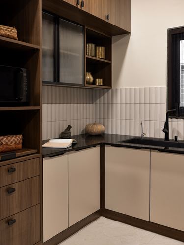 Corner kitchen with wood cabinetry, ribbed glass shutter, brass vessels, and black stone countertop