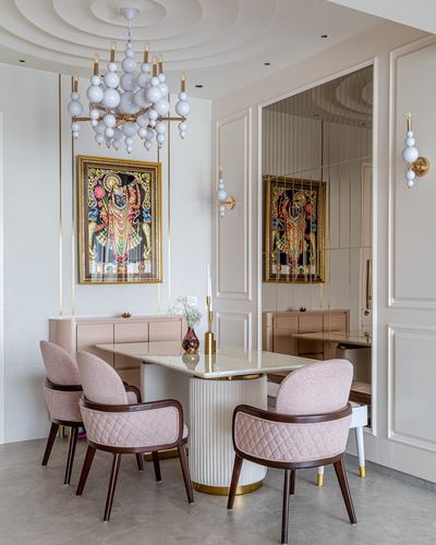 Pink dining room with round marble table, boucle chairs, brass chandelier and framed deity painting