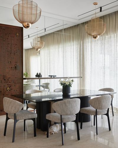 Dining room with black stone table, mesh pendant lights, and carved wooden jali screen