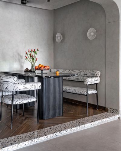 Dining nook with fluted stone table, patterned banquette seating and terrazzo threshold under a curved plaster archway