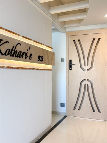 Entryway with backlit stone nameplate reading Kothari's 903 beside a carved wooden door