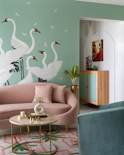 Blush curved sofa against mint wall painted with white swans, marble coffee table, arched doorway beyond