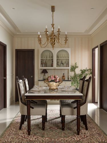 Symmetrical dining room with marble-top table, brass chandelier, and arched glass bar cabinet