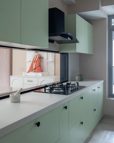 Sage green kitchen with black hob, chimney hood, and mirrored niche holding a deity idol