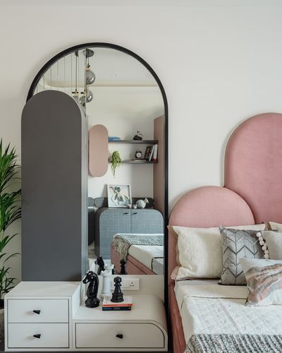 Arched mirror beside pink scalloped headboard with decorative chess pieces on white nightstand