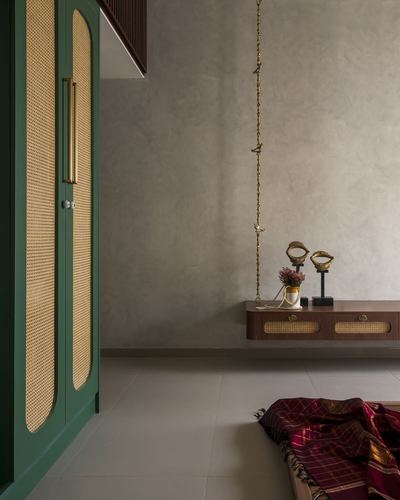 Green cane wardrobe beside a brass jhula chain and wooden console with brass figurines