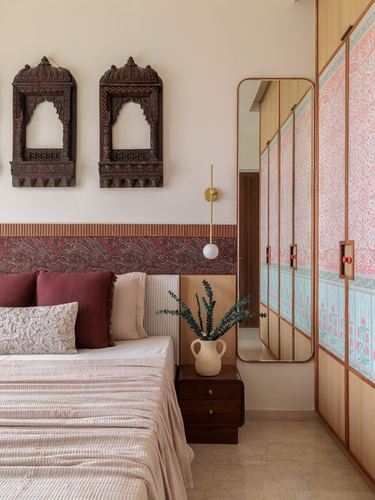 Bedroom with carved wooden wall pieces, floral wardrobe panels, and a tall mirror beside a bed