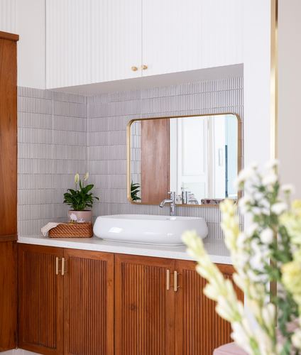 Bathroom vanity with wood fluted cabinets, oval basin, and brass-framed mirror on ribbed tile wall