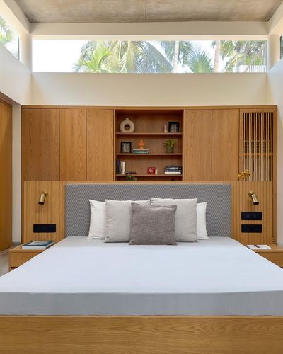Bedroom with wood-panelled headboard wall, open shelving niche, and clerestory windows showing palm trees