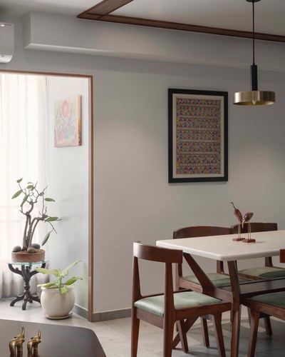 Dining nook with marble table, wooden chairs, framed folk art and brass pendant light