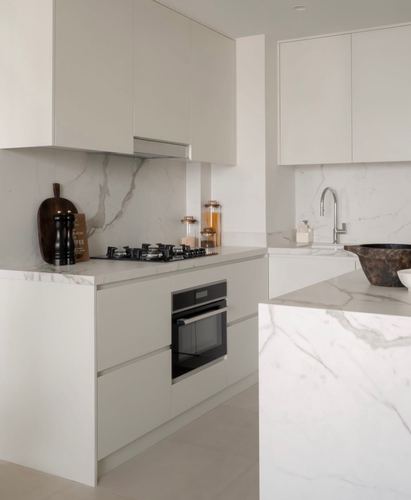 Minimalist white kitchen with veined marble countertops, backsplash, and waterfall island