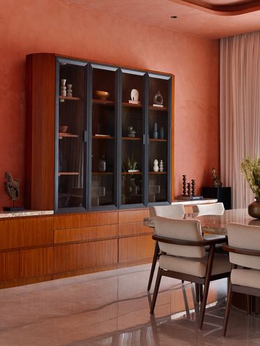 Terracotta dining room with wood cabinetry, glass display cabinet, and cane-backed dining chairs