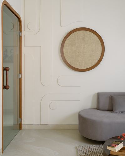 Living room corner with curved plaster wall art, round cane panel, glass door, and grey sofa