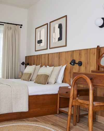 Bedroom with wood-panelled headboard wall, layered neutral pillows, and cane-seat wooden chair by vanity