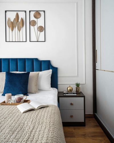Bedroom with navy velvet tufted headboard, beige linens, and a two-drawer bedside table with brass accents